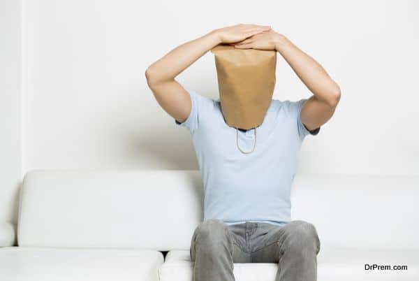 Miserable anonymous man with head covered sitting on sofa.