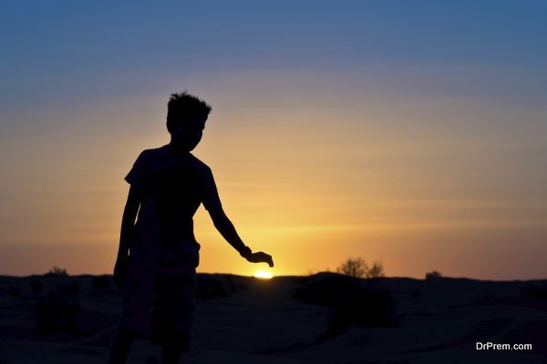 Silhouette of a boy covering the sun with his hand