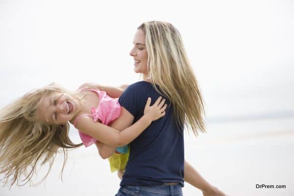 Mother swinging daughter over water at beach