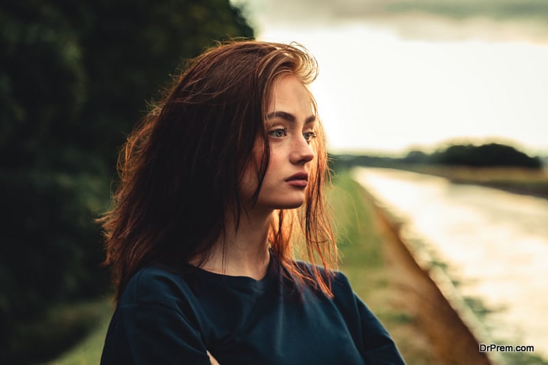 Young day dreaming, pensive and sad looking young woman standing alone outdoors 