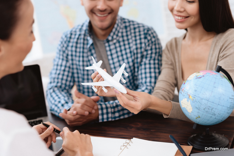 A young man and a woman came to the travel agency. The girl is holding a toy plane in her hands. They want to go on a trip during their holidays. The girl agent offers them different countries.