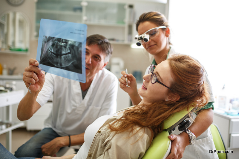 Dentists team in dental office discuss about teeth x-ray image with young female patient