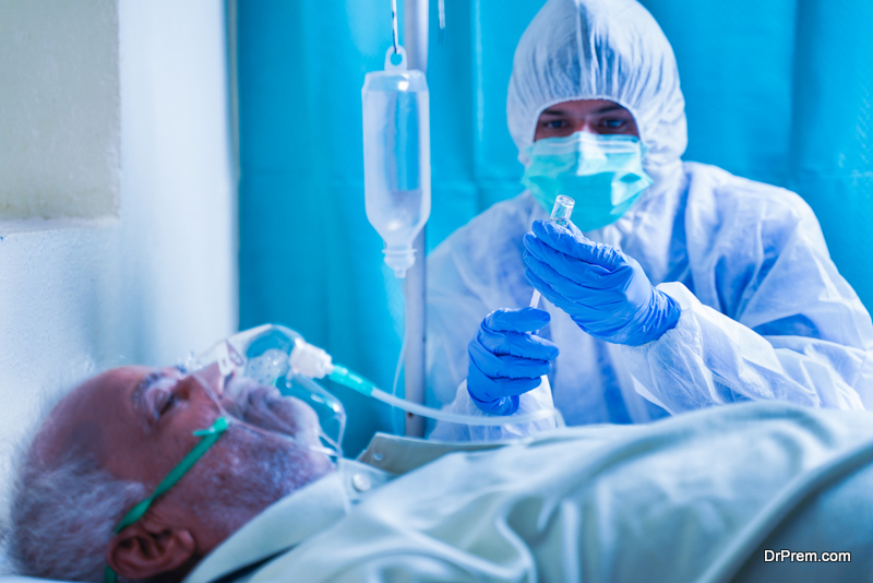 Doctor with protective suit preparing injection syringe while patient breathing on ventilator oxygen mask due to coronavirus covid-19 viral infection at hospital