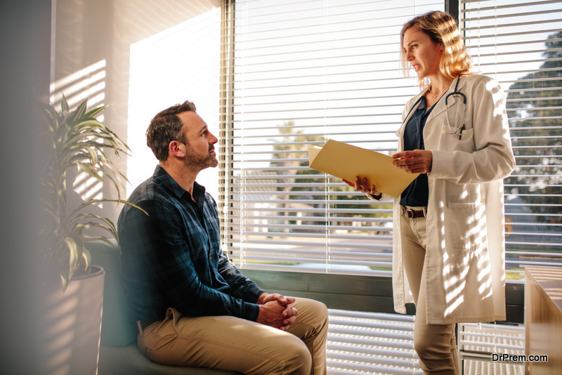 Female doctor holding a medical report file and talking with male patient sitting on sofa at hospital reception. Doctor explaining the treatment to patient.