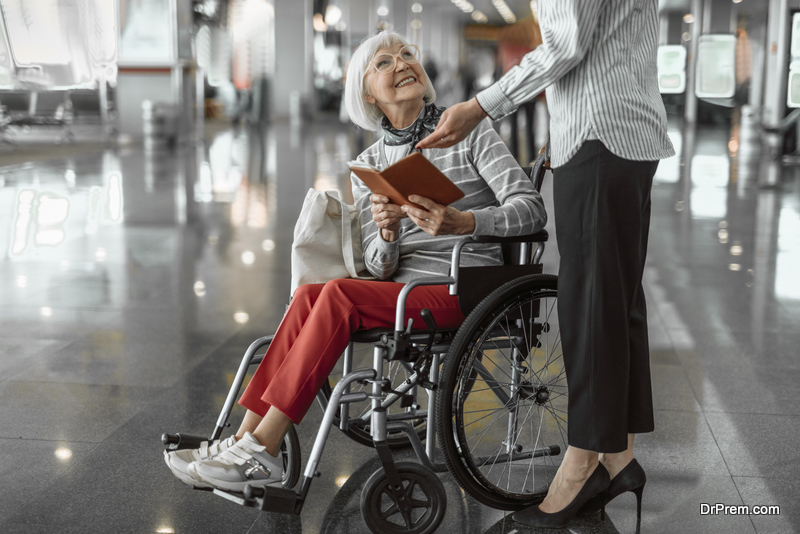 Female worker of airport talking to elderly woman in wheelchair 