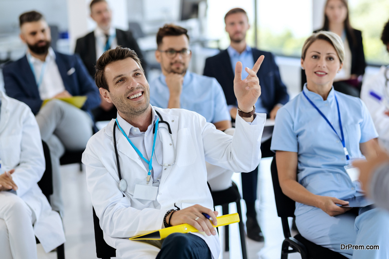 Happy doctor attending a seminar and raising his hand to ask a question at convention center