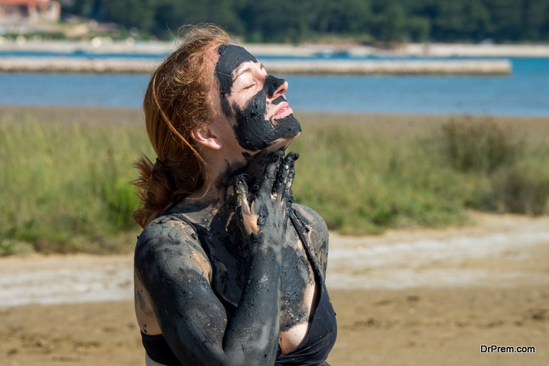 Red head covering her face, neck and body with the healing mud from the bay close to Soline, Croatia.