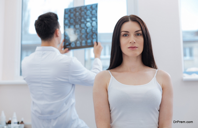 Serious beautiful nice woman standing and looking at you with a doctor checking her X ray 