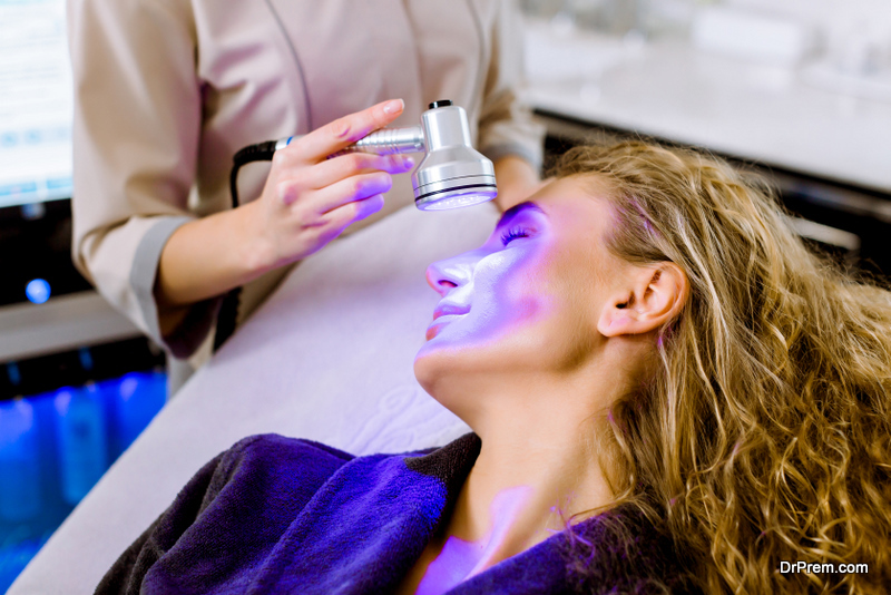 Skin Cosmetology. Woman beautician Doing Blue Light Therapy On face of pretty young blond woman.