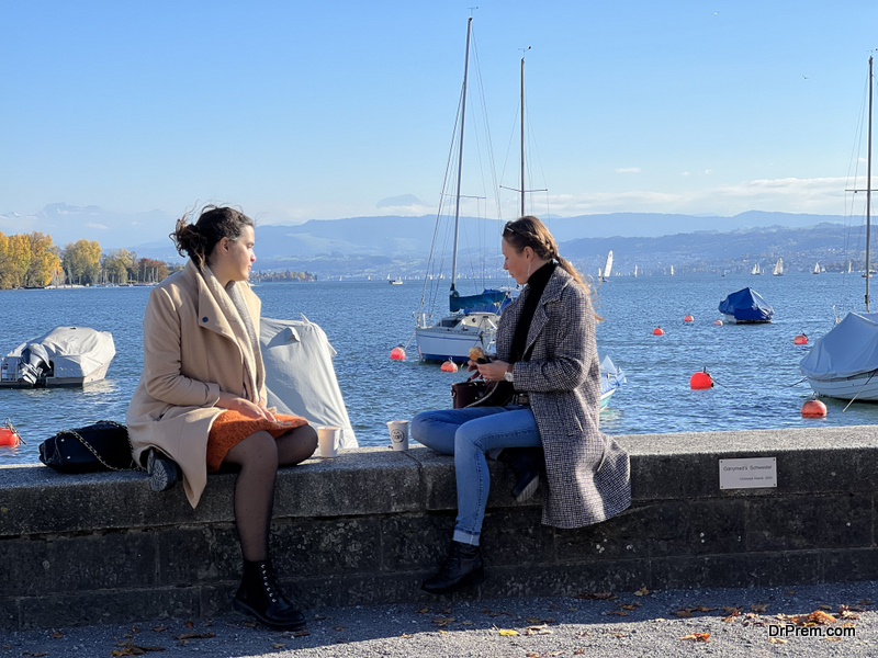 Zurich, Switzerland . Two female friends sitting on concrete barrier on lake Zurich in Switzerland.