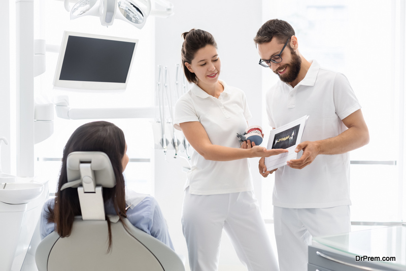 Two cheerful young dentist showing and explaining teeth disease treatment to patient