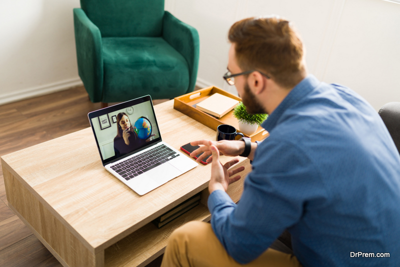 Rear view of a man at home having a video call with a female travel agent to book his travel or vacations