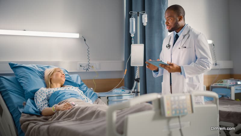 Hospital Ward Friendly Smiling Doctor Reassures, Talks to a Female Patient Resting in Bed.