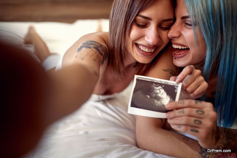 Cheerful homosexual female showing ultrasound image of future baby