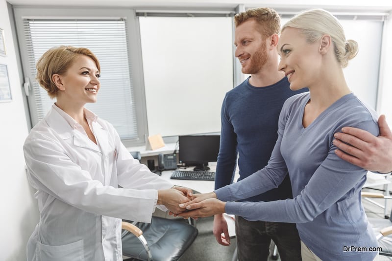 Smiling gynecologist is standing beside patients. She shaking hands with thankful woman