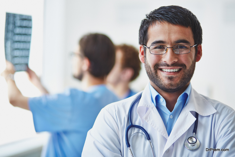 smiling doctor looking at camera on background of his working colleagues