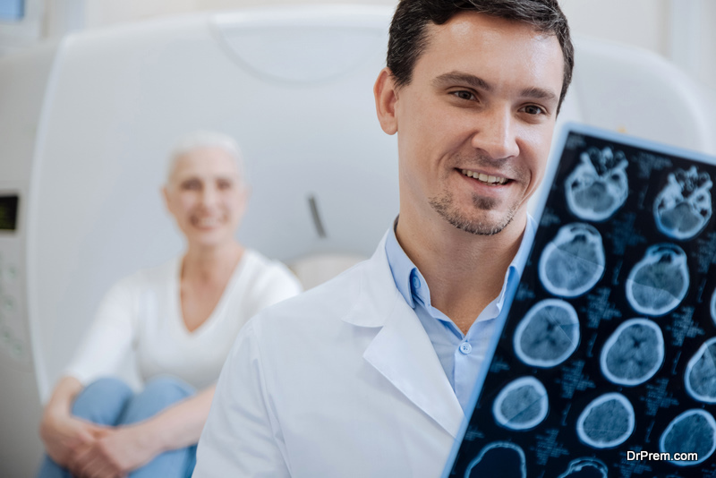 Happy positive male doctor holding CT scan results and smiling while looking at them