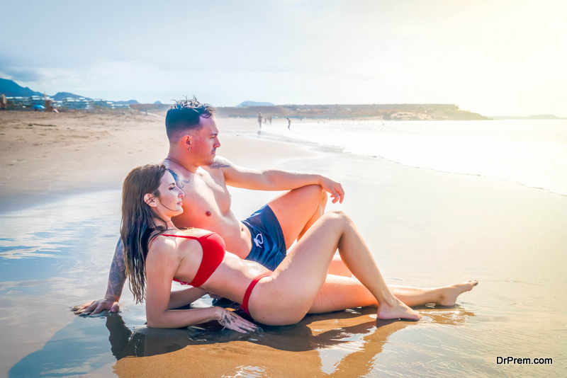 Happy young couple at the sea vacations, man and woman sunbathing and relaxing at the sea shore, vacations and honeymoon concept, toned