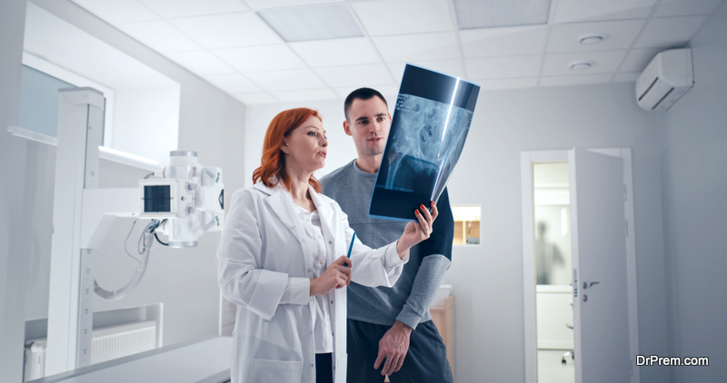 Middle aged woman in medical uniform demonstrating and explaining X ray image to adult man while working in lab in hospital