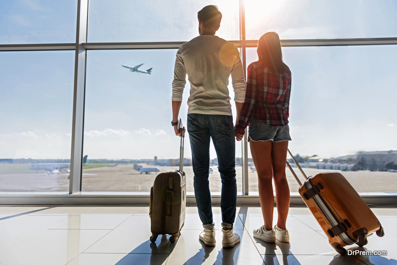 We are ready for new future. Young man and woman are watching flight at airport. They are standing and carrying luggage