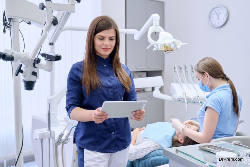 Portrait of young female doctor dentist with digital tablet in dental office, treating woman patient in chair background. Medicine, dentistry and health care concept