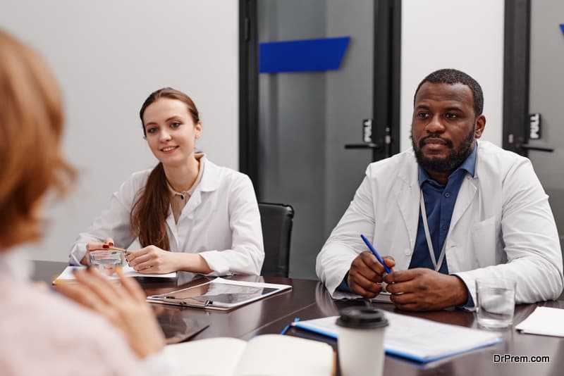 Two young intercultural healthcare experts in lab coats consulting colleagues about frequently asked questions concerning pandemic