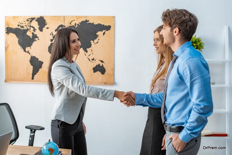 smiling travel agent shaking hands with happy man standing near girlfriend