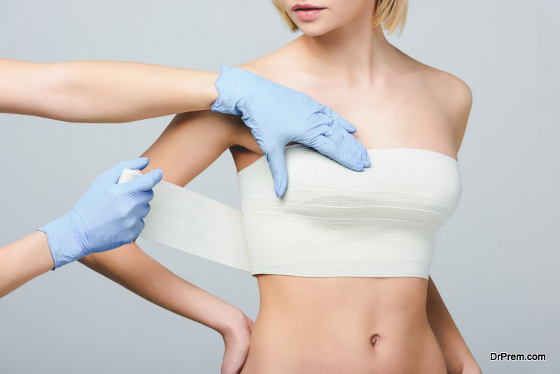 plastic surgeon wrapping female breast with bandage