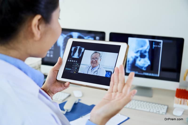 Senior male doctor discussing x-ray image or giving an instructions to his female assistant online on tablet pc at office