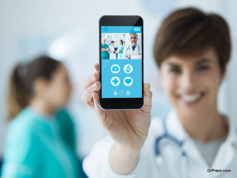 Smiling confident female doctor holding a touch screen smartphone and medical staff on the background, medical app concept