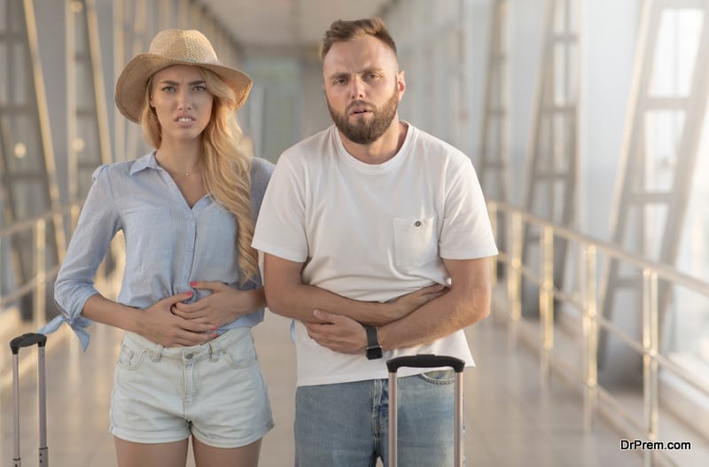 Couple suffering from stomachache, standing at airport terminal