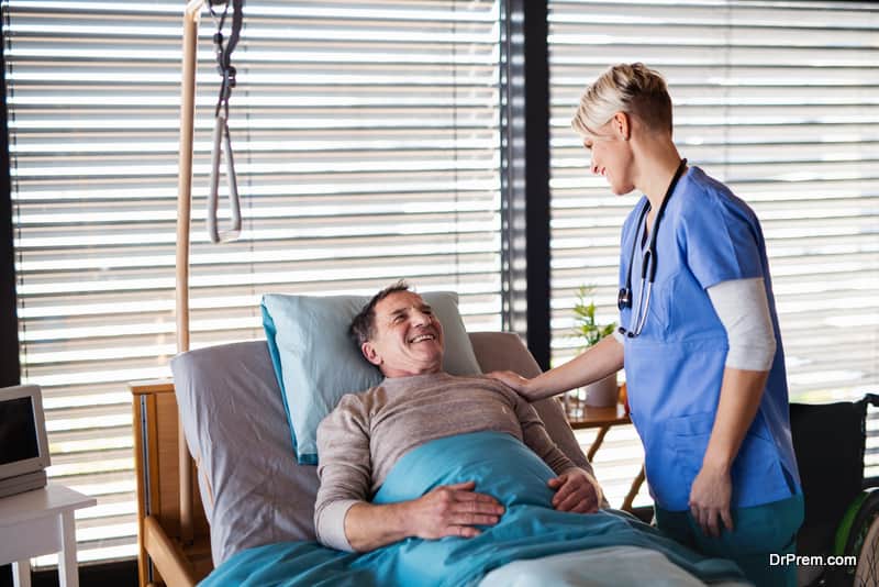 Friendly healthcare worker or nurse tallking to senior patient in bed in hospital.