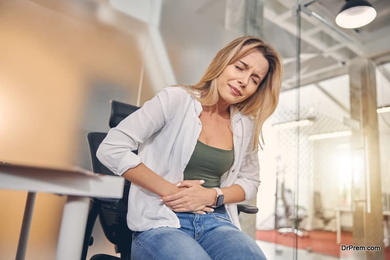 Unhappy blonde lady feeling pain in her stomach while sitting in chair 