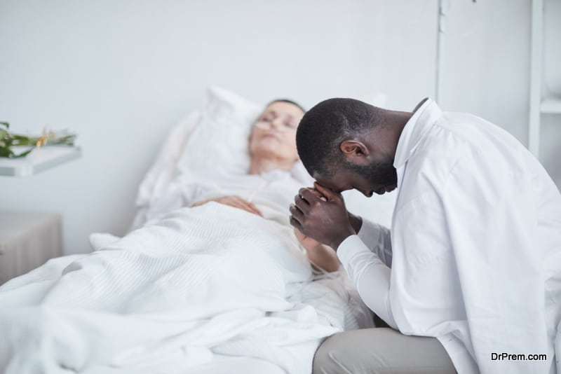 African sad man sitting in front of the hospital bed with his wife and worried about her health