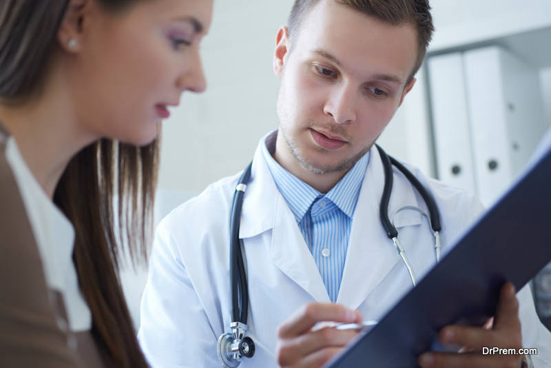 Handsome young doctor is holding a clipboard and talking with a female patient