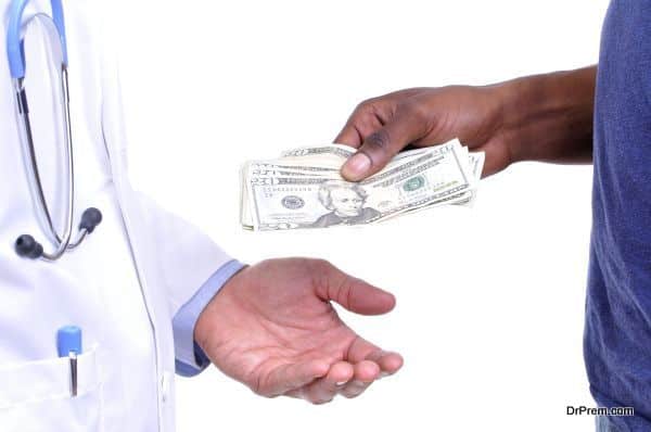 Closeup of hand of uninsured patient paying cash to hand of medical doctor wearing lab coat on white background