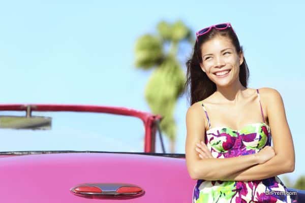 Car woman happy smiling by pink vintage car. Beautiful young multiracial female driver in Havana, Cuba.
