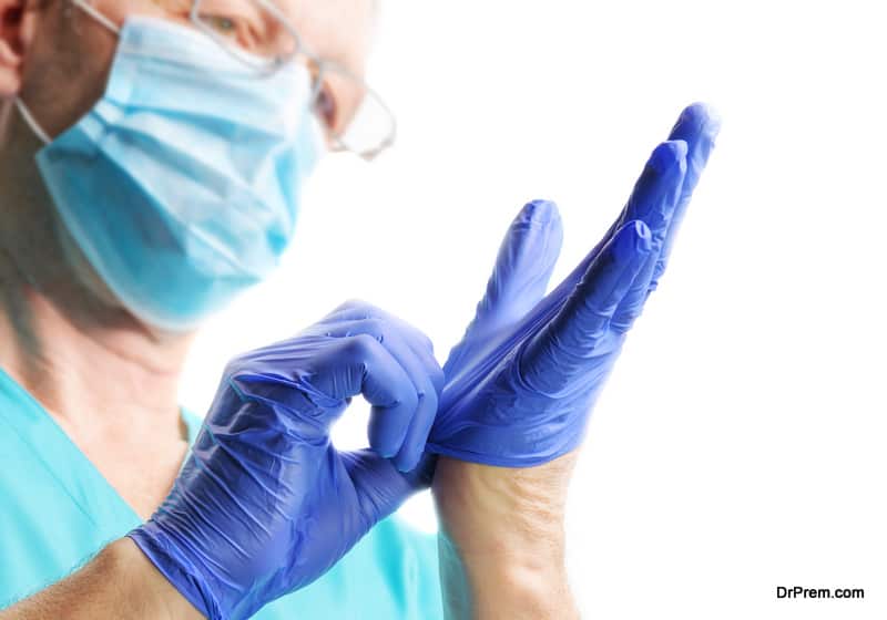 Doctor in medical mask putting on blue gloves