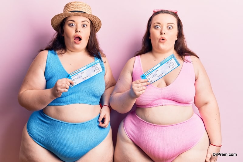 Young plus size twins wearing bikini holding boarding pass scared and amazed with open mouth for surprise, disbelief face