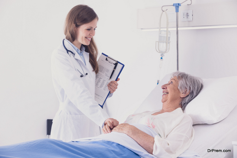 Smiling female doctor or nurse comforting an elderly woman patient in a bed reaching out to hold her hand during ward rounds at a hospital