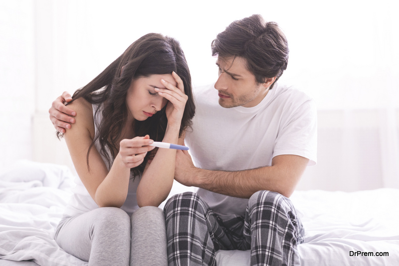 Upset man comforting his depressed wife with negative pregnancy test, free space