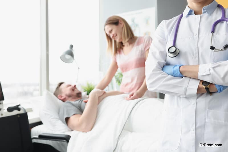 Happy man lies on hospital bed his hand is held by woman next to doctor. 