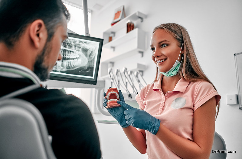 Female-dentist-holding-teeth-model-denture-showing-and-explaining-to-patient-at-clinic