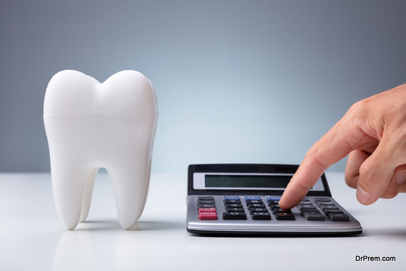 Person Calculating Expenses Near Tooth Model Over White Desk