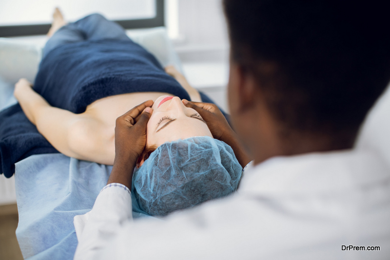 shoulder of African male masseur of young woman enjoying anti aging facial massage