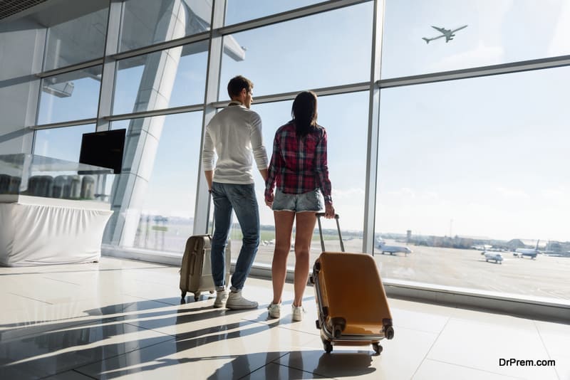 Young man and woman are looking through window at airport 