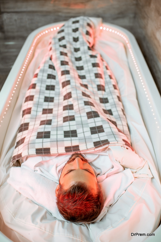Man lying in the hot SPA capsule wrapped with bedcover during the mud wrap procedure in the SPA salon