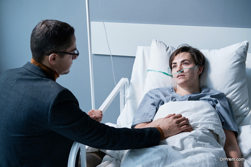 young man supporting the sick young woman while she lying on bed at hospital ward