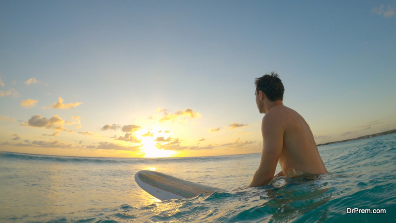 Young Caucasian man on surfing vacation in picturesque Barbados sits on his surfboard and watches the sunset