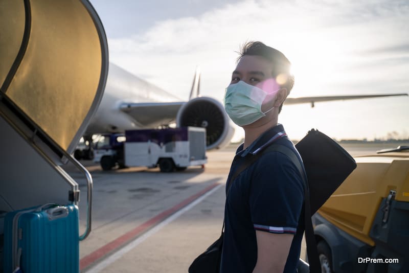 Asian man wearing face mask walks to stair entering airplane, 